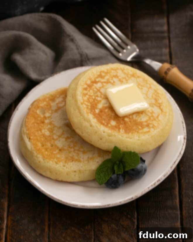 Two freshly cooked buttermilk pancakes resting on a white plate, topped with a pat of butter, ready to be served.