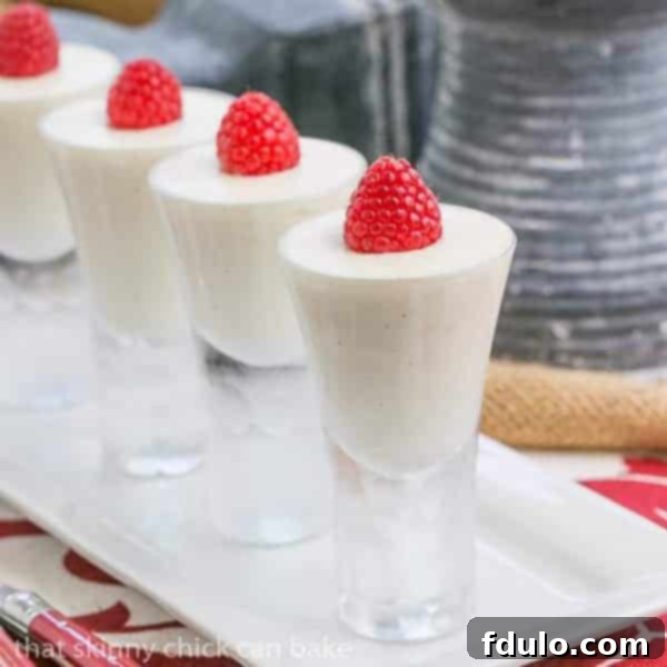 Vanilla Bean Cheesecake Shooters topped with fresh raspberries on a pristine white tray, highlighting their elegant presentation and vibrant color.