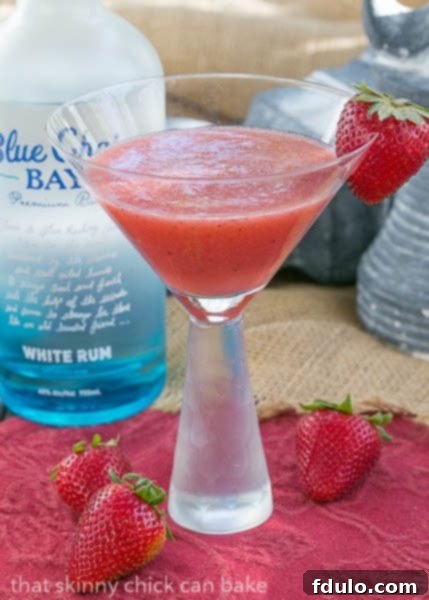 Hawaiian Sunset Cocktail - Strawberries, pineapple and rum form an irresistible tropical drink Hawaiian Sunset Cocktail with a strawberry garnish in front of a bottle of rum
