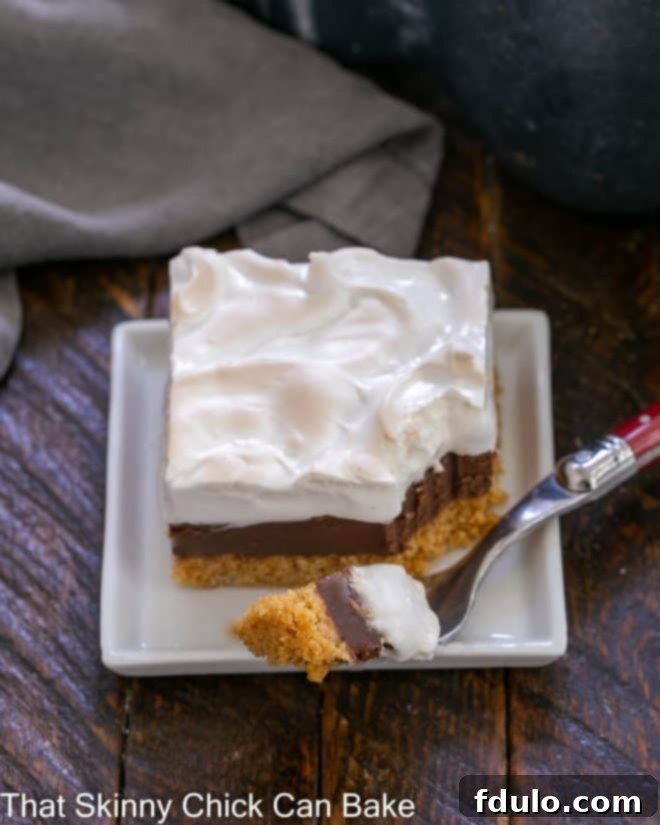 A S'mores Fudge Bar on a white plate with a piece on a red-handled fork, showcasing its soft, toasted meringue.