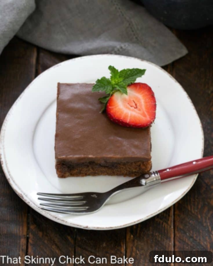 overhead view of coca cola cake on a round white plate with a strawberry slice to garnish and a red handled fork