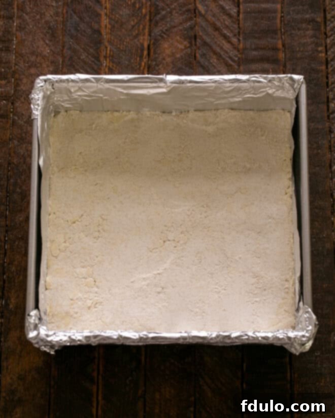 Step 2: Gently pressing the crumbly shortbread crust mixture evenly into a prepared baking pan, creating a solid base for the blueberry bars.