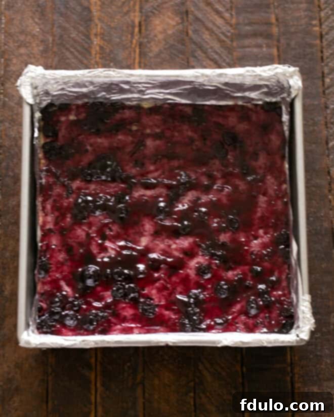 Step 4: Spreading a rich, vibrant blueberry jam evenly over the pre-baked shortbread crust, creating a sticky, flavorful base for the fresh blueberries.