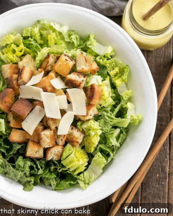 Perfect Caesar Salad - Make your favorite restaurant salad at home! Freshly prepared Caesar Salad in a white serving bowl with wooden tongs, ready to be served. A jar of homemade Caesar dressing is beside it.