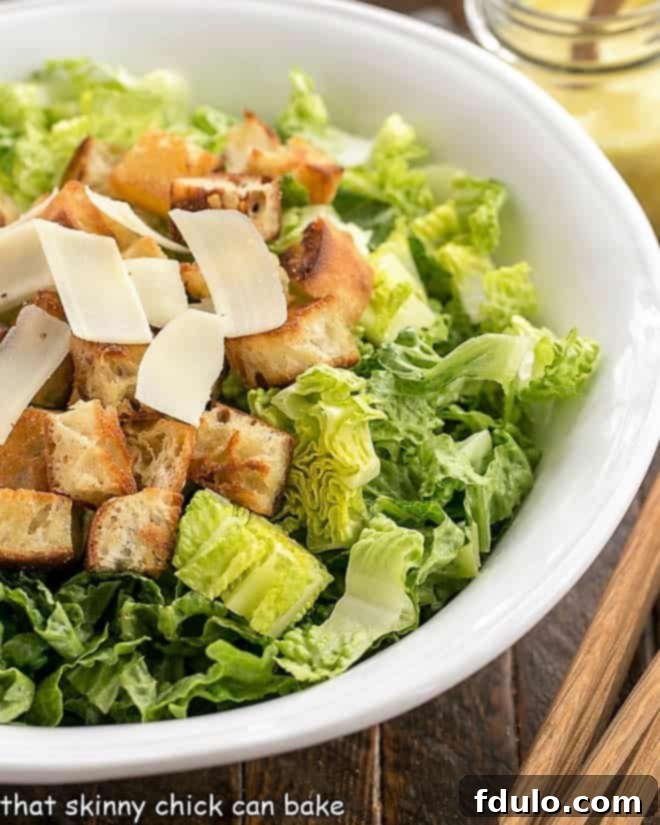 The Best Caesar Salad - the classic restaurant salad that you can easily make even better at home! Close-up view of undressed Caesar salad ingredients (romaine, croutons, Parmesan) in a white serving bowl, ready for dressing.