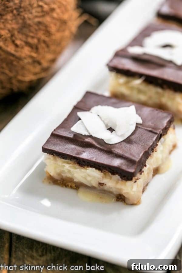 Close-up shot of homemade Coconut Bars on a white ceramic tray, showing the intricate layers and rich chocolate topping.