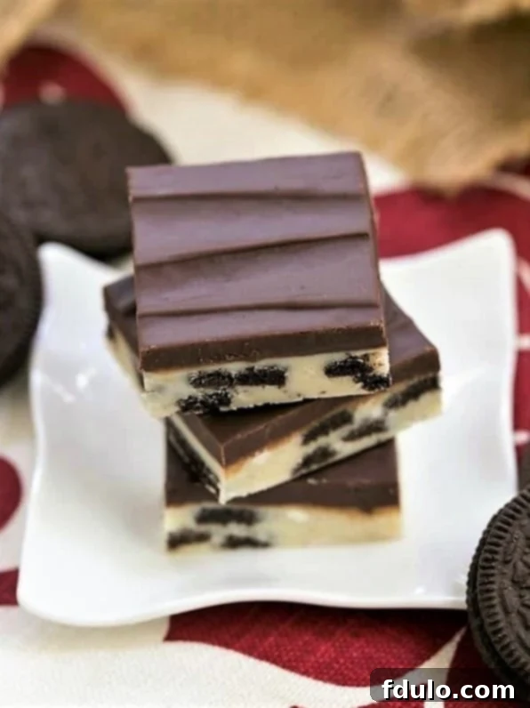Oreo Double Decker Fudge stacked on a small white ceramic plate surrounded by whole and broken Oreos.