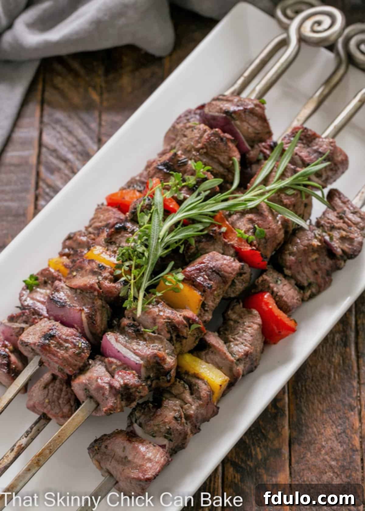Overhead view of lamb kabobs on a white platter with an herb garnish, showcasing perfectly grilled, tender lamb pieces.