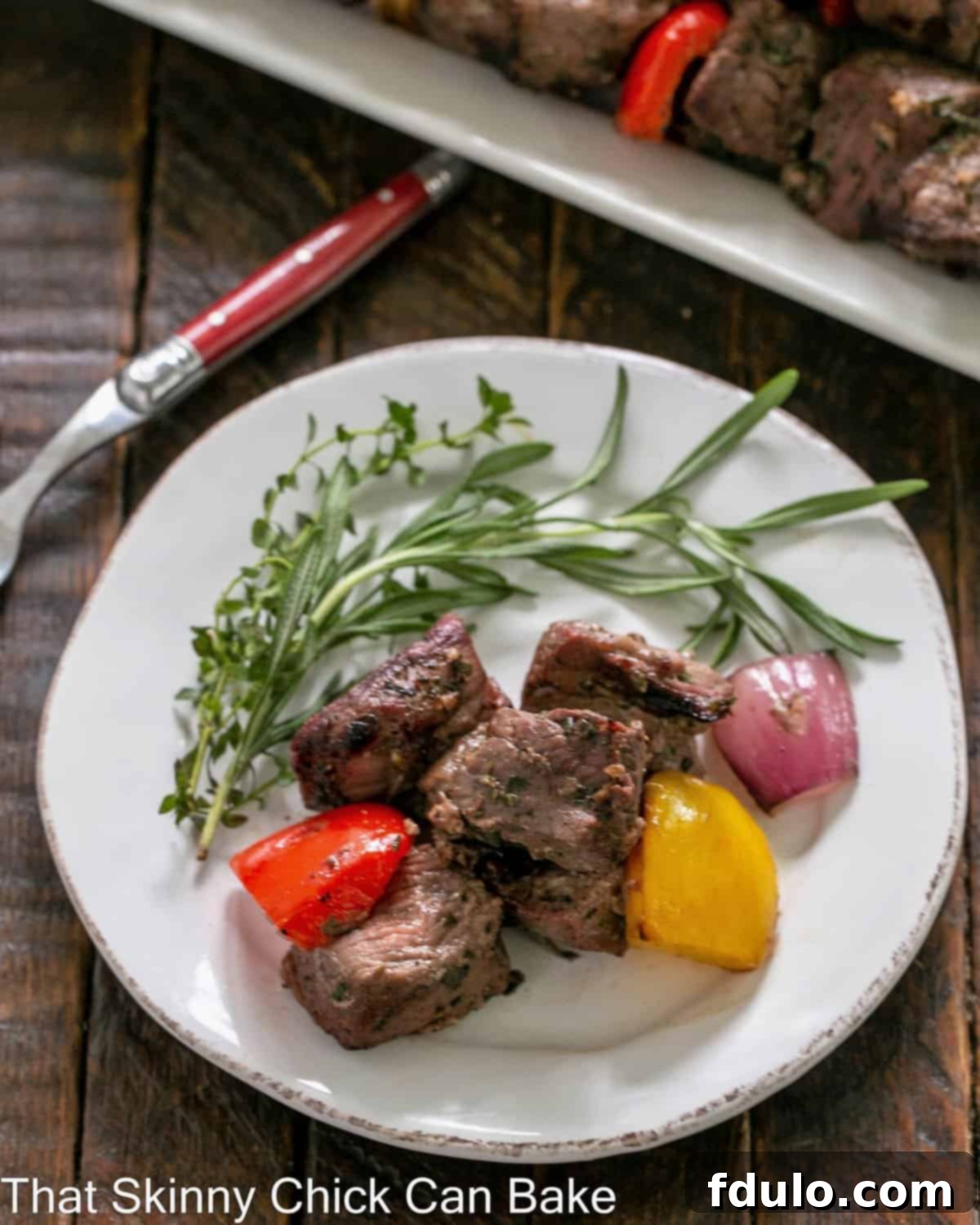 Overhead view of grilled lamb off the skewers on a round white plate with fresh herbs for garnish.
