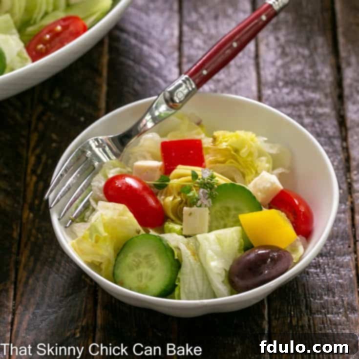 Small white bowl of Greek salad with a red handled fork, featuring fresh vegetables and feta cheese.