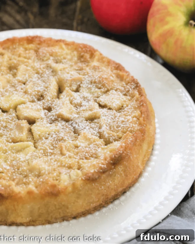 Uncut French Apple Cake on a white cake plate, golden brown and inviting.