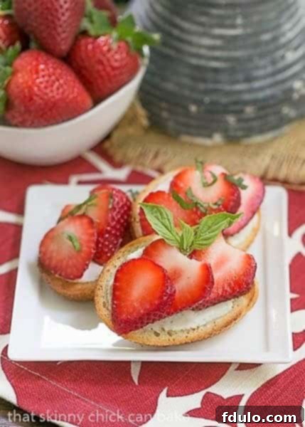 Close-up of Strawberry Basil Crostini arranged on a white appetizer plate next to a bowl of fresh strawberries and basil leaves, ready for serving