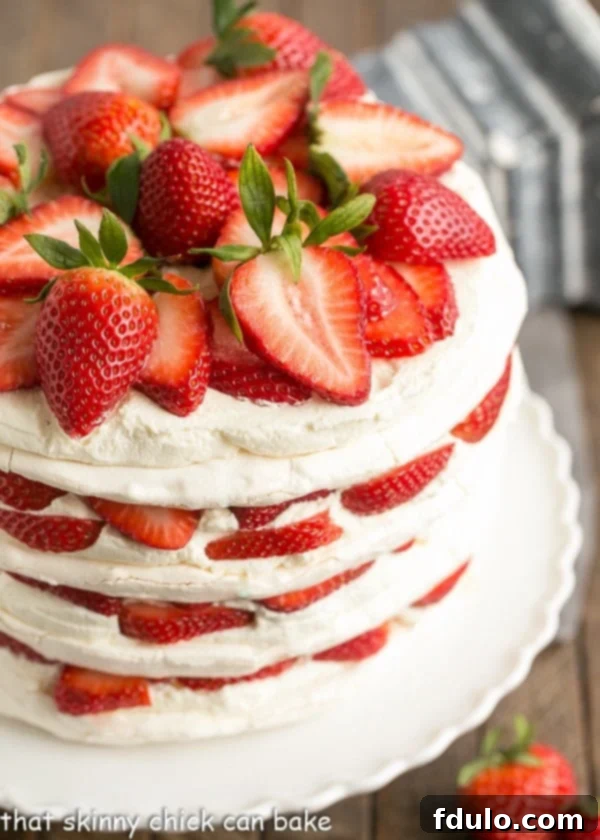 Fresh Strawberry Meringue Cake - A luscious dessert with layers of baked meringue, fresh strawberries and mascarpone whipped cream! Side view of Fresh Strawberry Meringue Cake on a white porcelain cake stand.