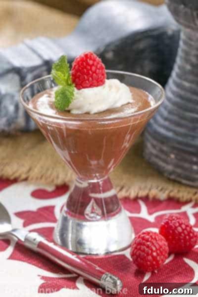 Decadent French chocolate mousse elegantly garnished with fresh whipped cream, a vibrant raspberry, and a sprig of fresh mint.