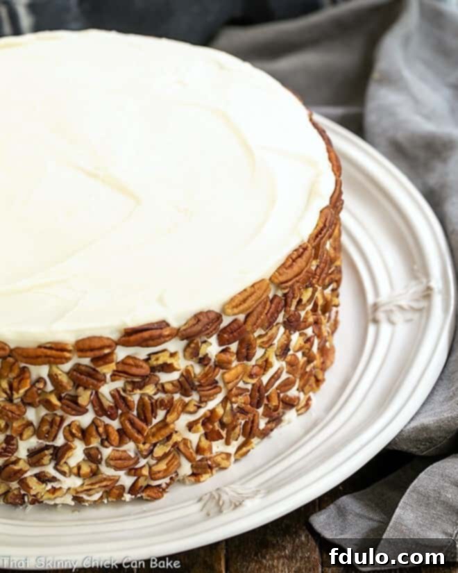 Best Carrot Cake Recipe - Dense and full of coconut, pecans and pineapple, then topped with decadent cream cheese frosting Classic Carrot Cake with pecans garnishing the sides, presented on a white serving plate.