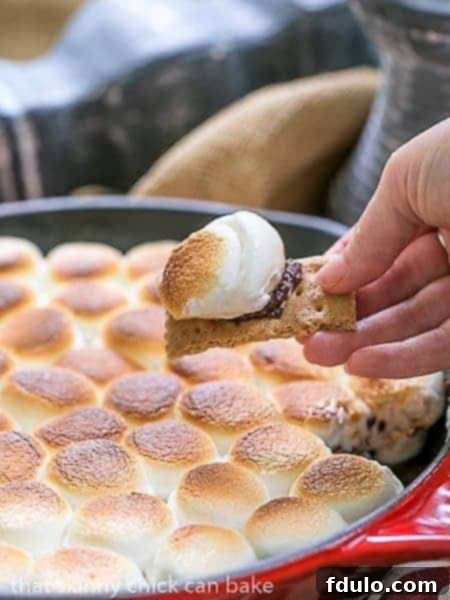 A close-up view of the golden-brown Skillet S'mores Dip with a perfect scoop of melted chocolate and toasted marshmallow on a graham cracker.