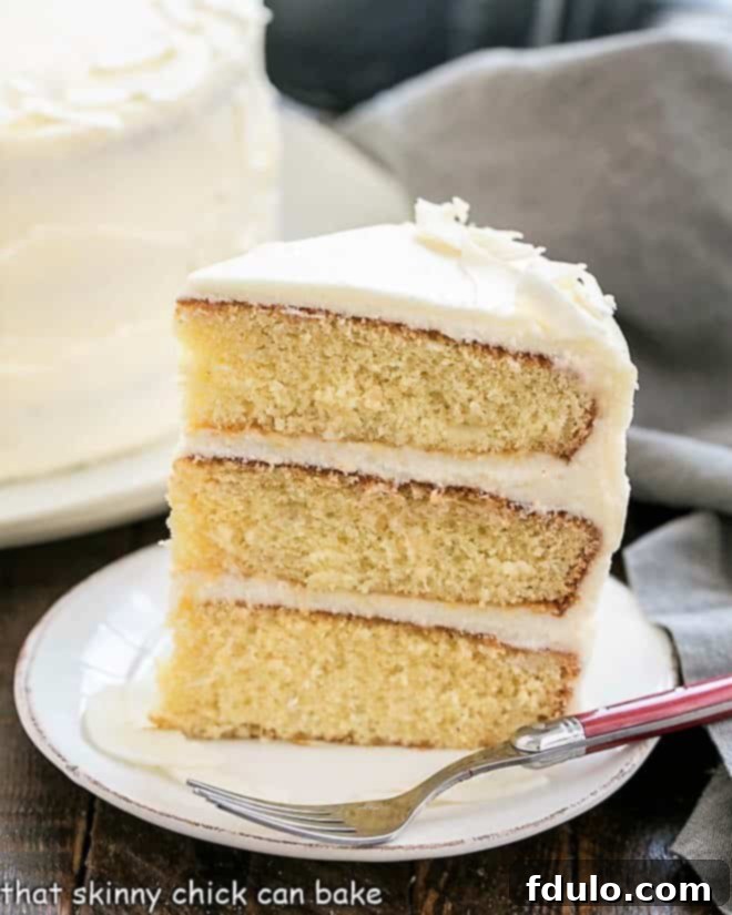 A perfectly sliced piece of Italian Cream Cake, showcasing three moist coconut layers and rich cream cheese frosting, on a white dessert plate.