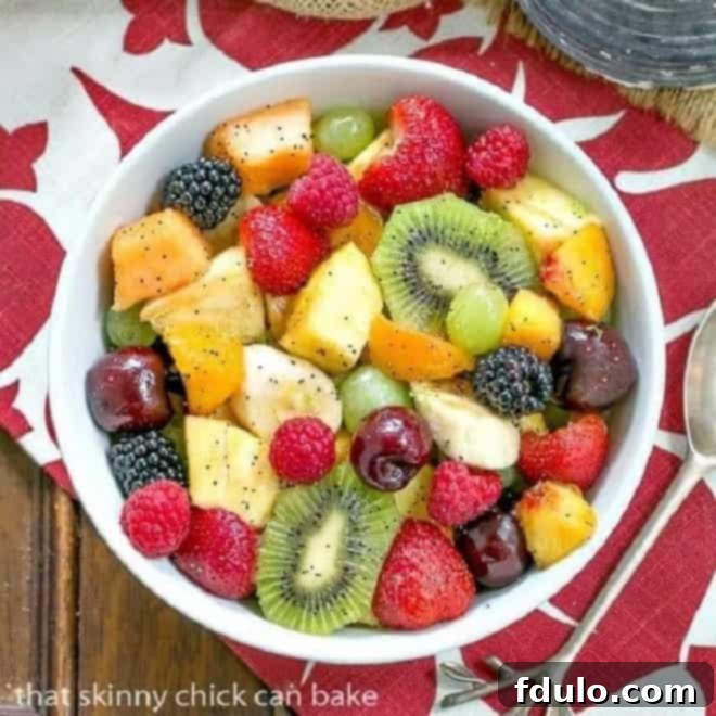 Overhead view of honey lime fruit salad in a white ceramic bowl on a red and white pattern napkin.