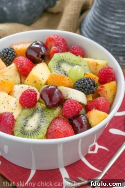 A white bowl of colorful fresh fruit with poppyseet dressing on a red and white napkin.