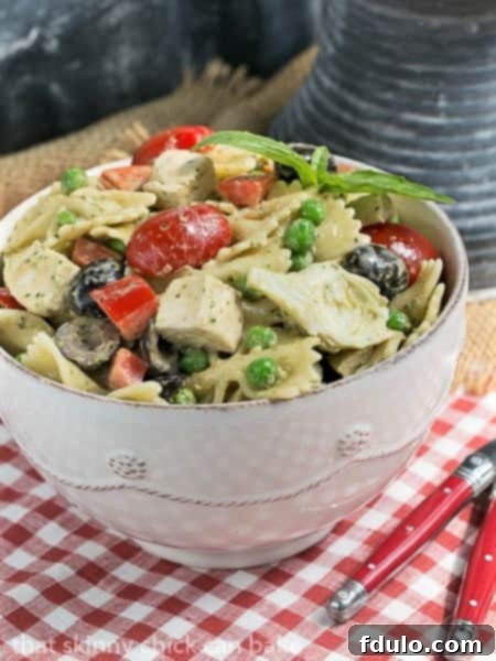 Close-up shot of Pesto Pasta Salad in a white bowl, garnished with fresh basil leaves, accompanied by two red-handled forks.