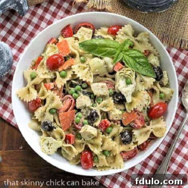 Overhead view of a beautifully arranged Pesto Pasta Salad in a white bowl, placed on a classic red and white checkered napkin.