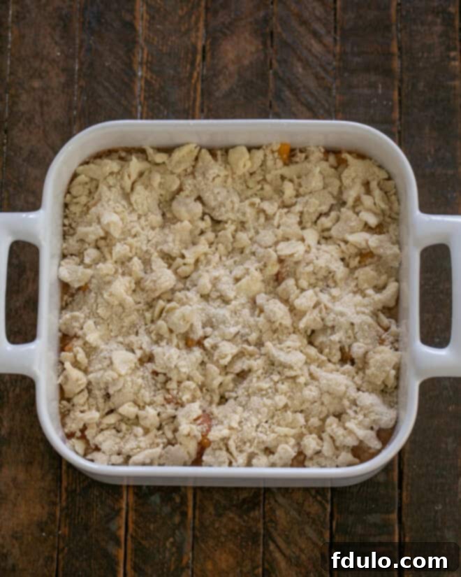 Crumble topping being sprinkled over the peaches in a baking dish.