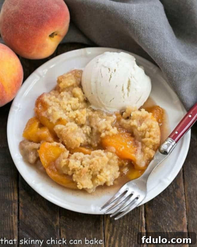 A slice of Classic Peach Crisp on a plate with vanilla ice cream.