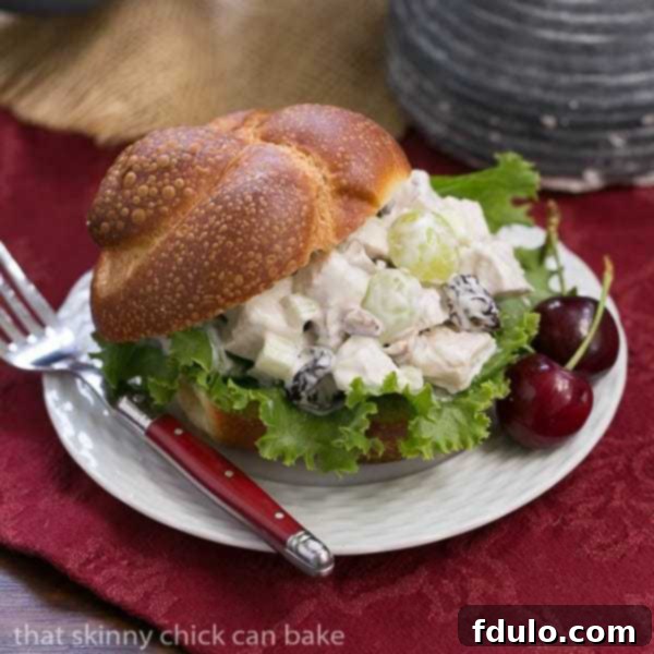 A plate of gourmet chicken salad on a soft bun, garnished, over a vibrant red napkin.