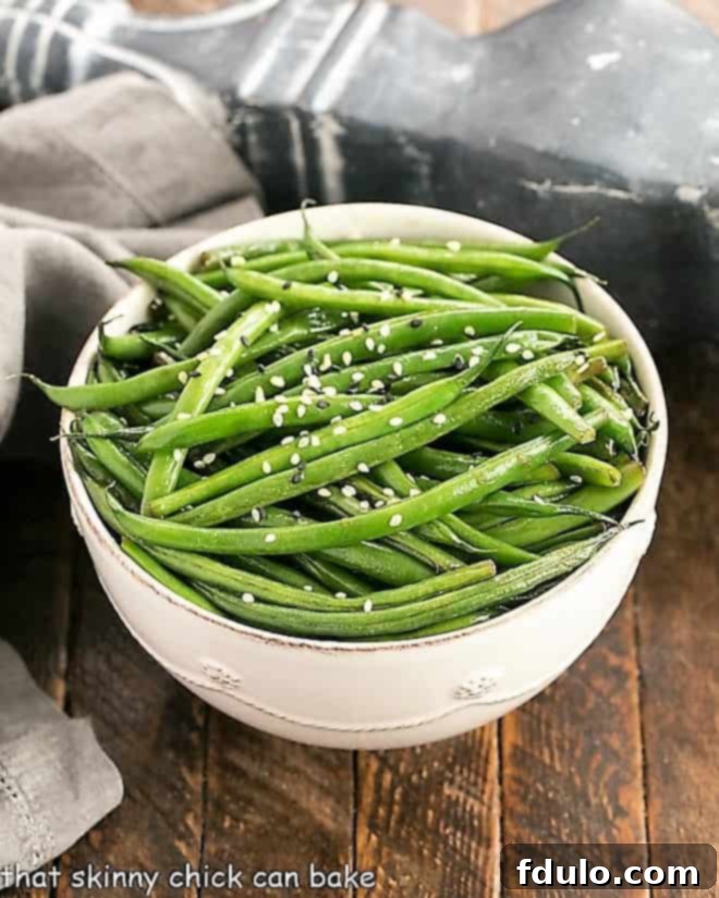 Asian Green Beans overhead view in a white ceramic bowl, garnished with sesame seeds.