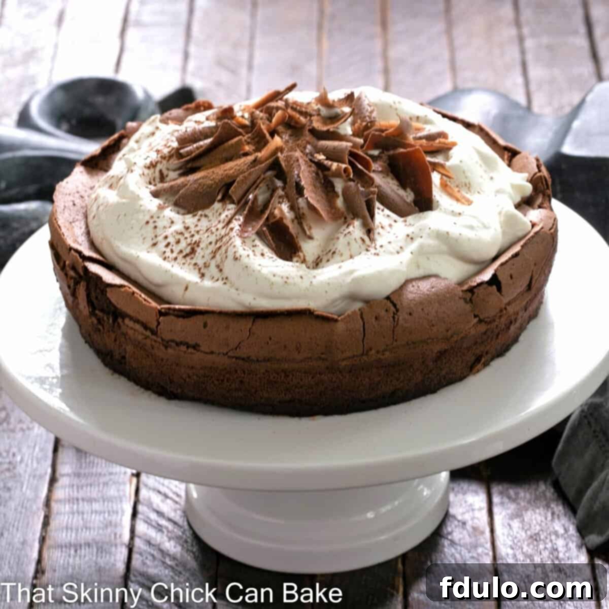 Velvet Chocolate Souffle Cake 4 A perfectly baked Chocolate Souffle Cake, with its signature crackled top and a generous dollop of whipped cream, on a white ceramic cake stand.