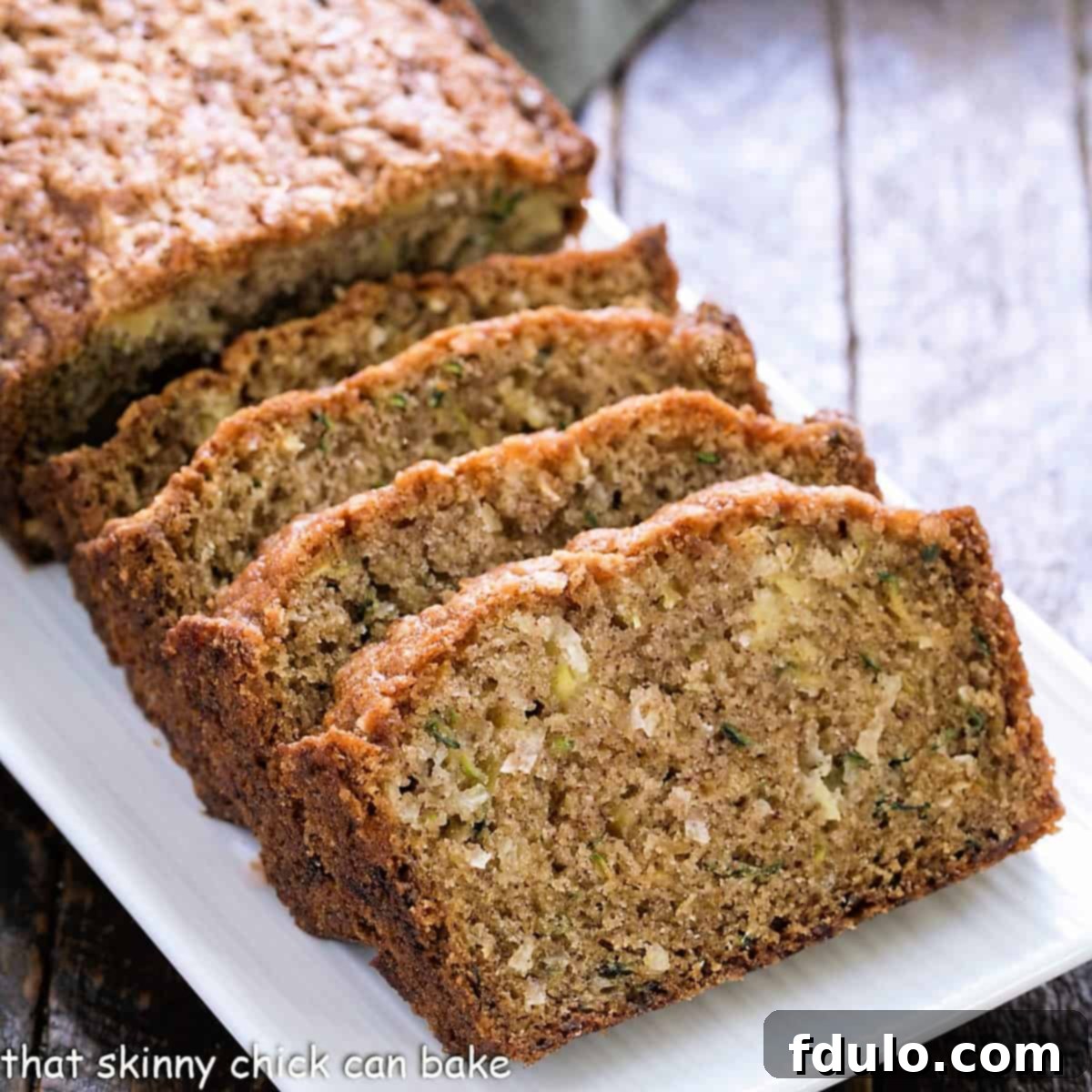 Two slices of golden-brown Pineapple Coconut Zucchini Bread on a white plate, showcasing the moist texture and speckles of coconut and pineapple.