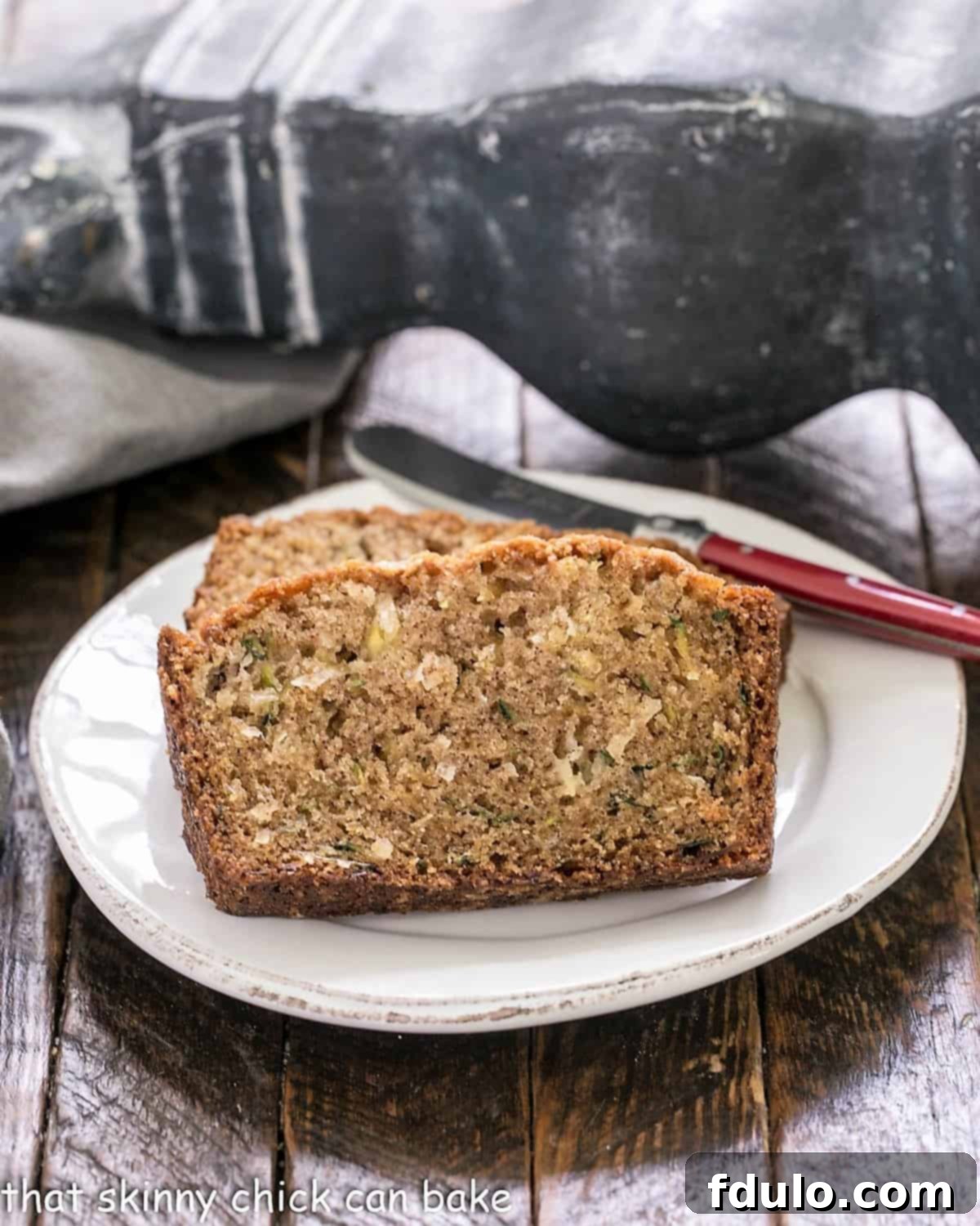Slices of delicious zucchini bread on a white plate with a red handled knife, ready to be enjoyed.