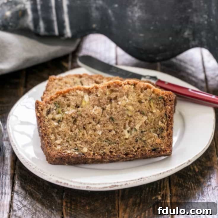 A perfectly sliced loaf of Pineapple Coconut Zucchini Bread on a white plate with a red handled knife, ready to be served.