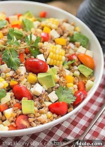Vibrant Summer Farro Salad with corn, avocado, and Cotija cheese in a white bowl, resting on a checkered napkin.