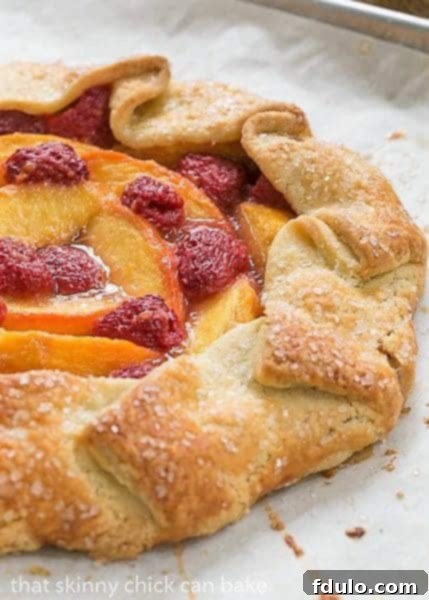 A freshly baked Peach Raspberry Galette resting on parchment paper on a baking sheet, showcasing its golden crust and bubbling fruit filling.