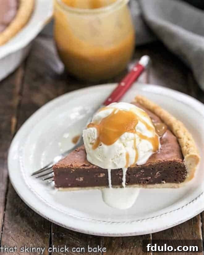 Fudgy Brownie Pie - Rich brownie filling studded with chocolate chips and baked in a flaky pastry shell! A close-up shot of a slice of Fudgy Brownie Pie topped generously with a scoop of vanilla ice cream and a luscious caramel sauce.