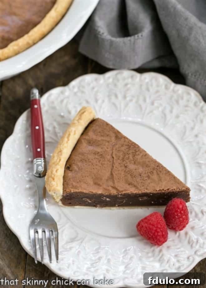 Fudgy Brownie Pie - Rich brownie filling studded with chocolate chips and baked in a flaky pastry shell! A beautifully presented slice of Fudgy Brownie Pie on a fancy white plate, garnished with fresh raspberries and a red handled fork resting beside it.