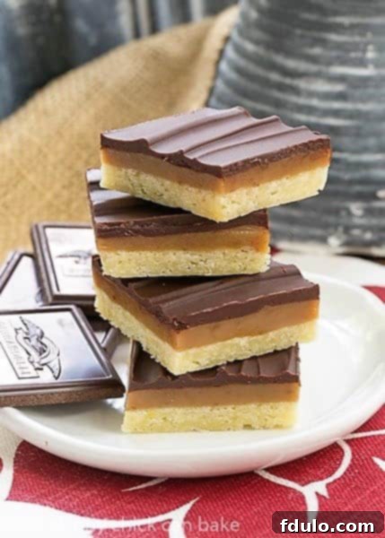 Ganache Topped Caramel Bars stacked high on a white plate over a red and white napkin, looking incredibly inviting.