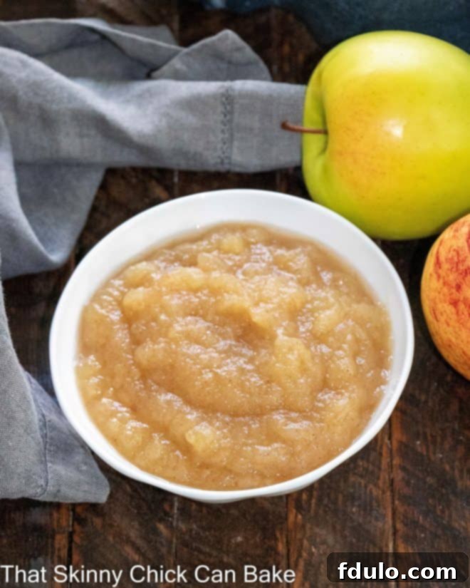Overhead view of small bowl of apple sauce next to 2 apples.
