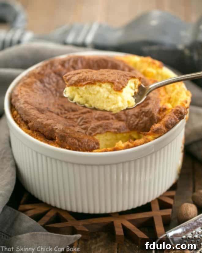A spoonful of French Gruyere Souffle scooped out, showcasing its light and fluffy texture, with the souffle dish in the background.