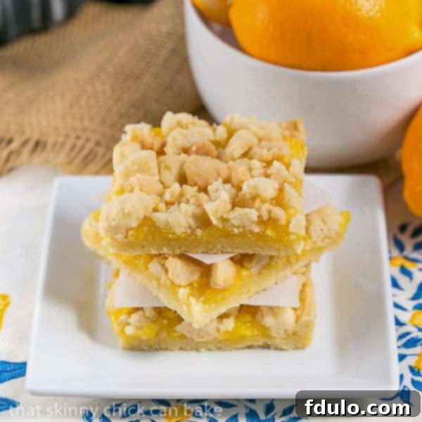 Meyer Lemon Streusel Bars - A scrumptious lemon bar with a sugar cookie crumble topping A stack of Meyer Lemon Streusel Bars on a square white plate, showing the golden streusel and bright lemon filling.