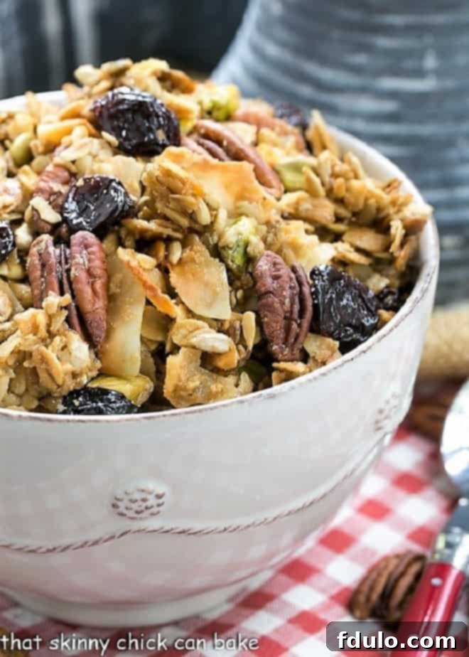 Homemade Granola Recipe - An irresistible granola sweetened with maple syrup and full of nuts, seeds and dried cherries A close-up shot of golden-brown Maple Coconut Granola in a pristine white ceramic bowl, showcasing the rich texture of oats, coconut flakes, nuts, and seeds.