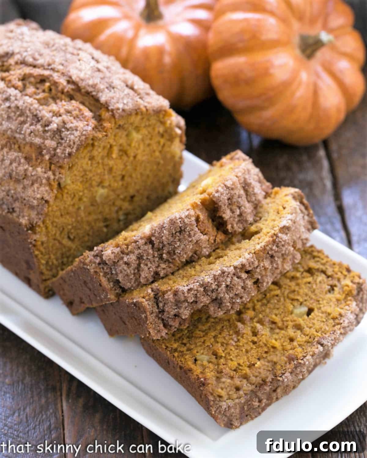 Pumpkin Bread with Apples sliced on a white ceramic tray with 2 mini pumpkins.