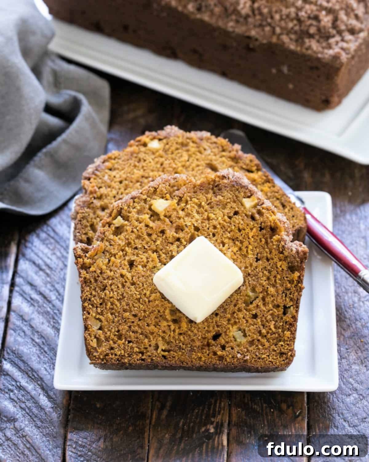 2 slices of an easy pumpkin bread on a white plate in front of a loaf of pumpkin bread on a tray.