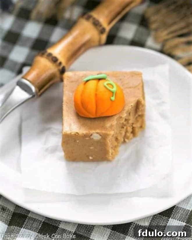 Easy Pumpkin Fudge on a white plate, topped with a decorative candy pumpkin, with a fork removing a piece.