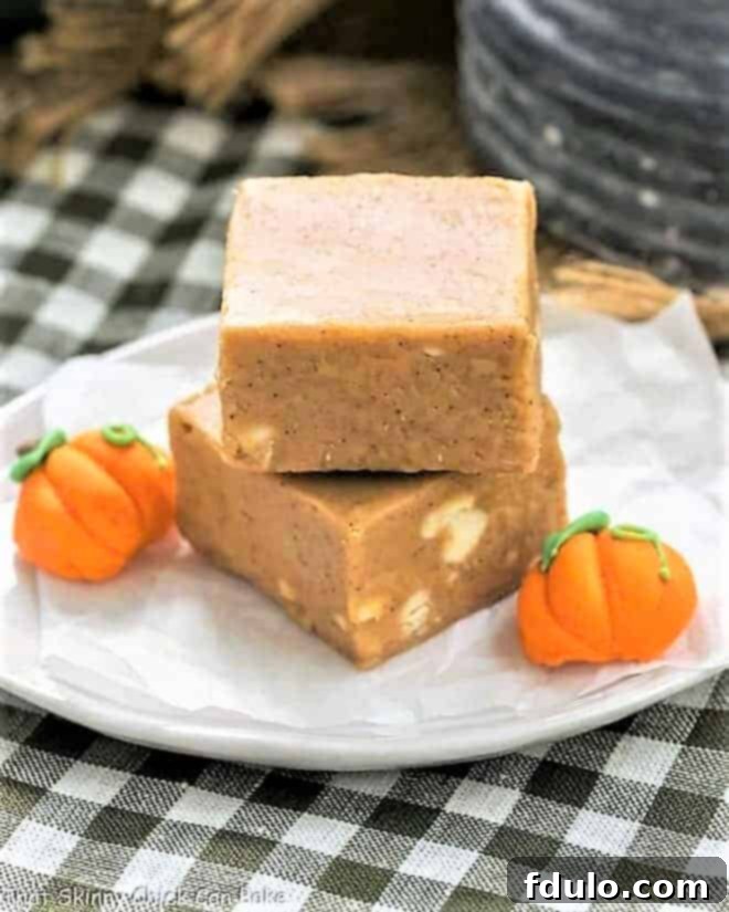 Easy Pumpkin Fudge squares stacked on a white plate with small candy pumpkins, ready for serving.