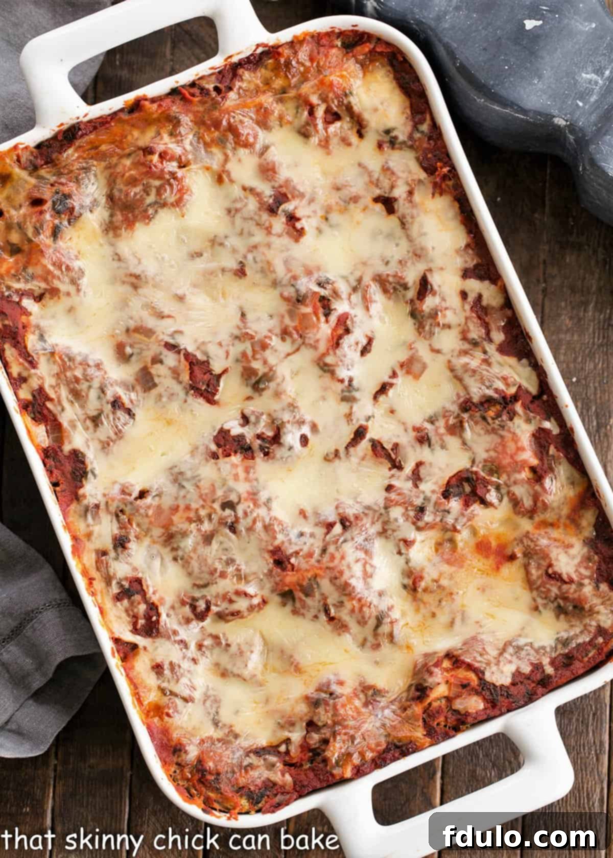 An overhead view captures the vibrant layers of a freshly baked Easy Spinach Lasagna, nestled in a pristine white casserole dish, with golden-brown cheese bubbling around the edges, promising a rich and comforting experience.