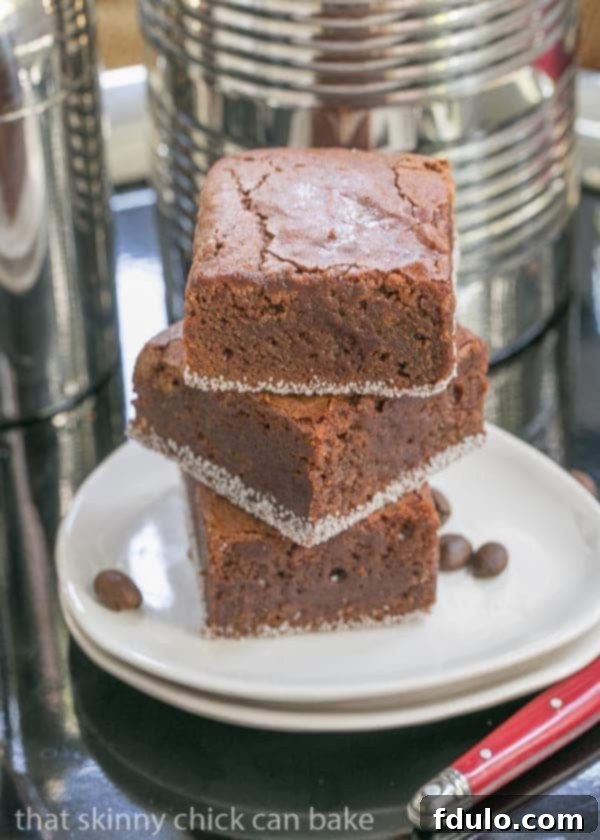 Fudgy Mocha Brownies - Delivering an irresistibly dense and decadent chocolate-coffee flavor! A stack of three rich Fudgy Mocha Brownies resting on elegant oval white plates.