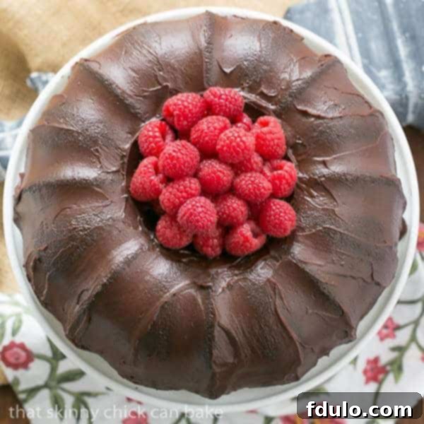 Decadent Chocolate Buttermilk Bundt Cake adorned with fresh raspberries, presented on a pristine white cake stand.