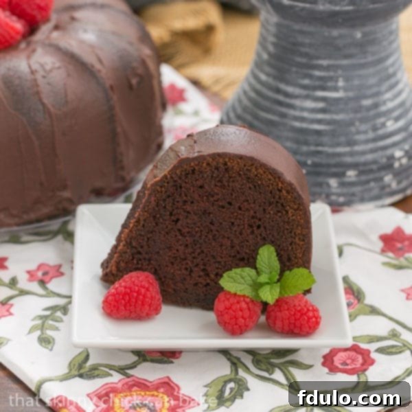 A slice of Chocolate Buttermilk Bundt Cake rests on a square white dessert plate, revealing its moist, dark interior.